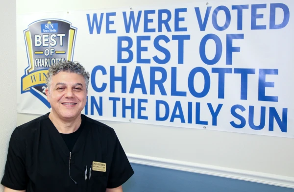 Dr. Tim standing by a sign saying "We were voted best of Charlotte in the Daily sun"